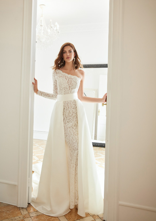 In questa foto una modella mentre esce da una porta indossando un abito da sposa in pizzo all over con sovragonna di Inmaculada Garcia 2023   