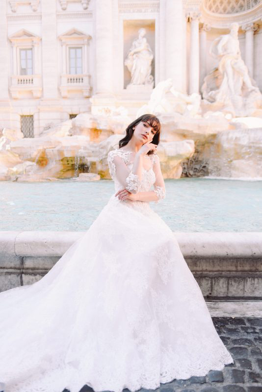In questa foto una modella posa davanti alla Fontana di Trevi, a Roma, indossando un abito de Le Spose di Andrea 2023