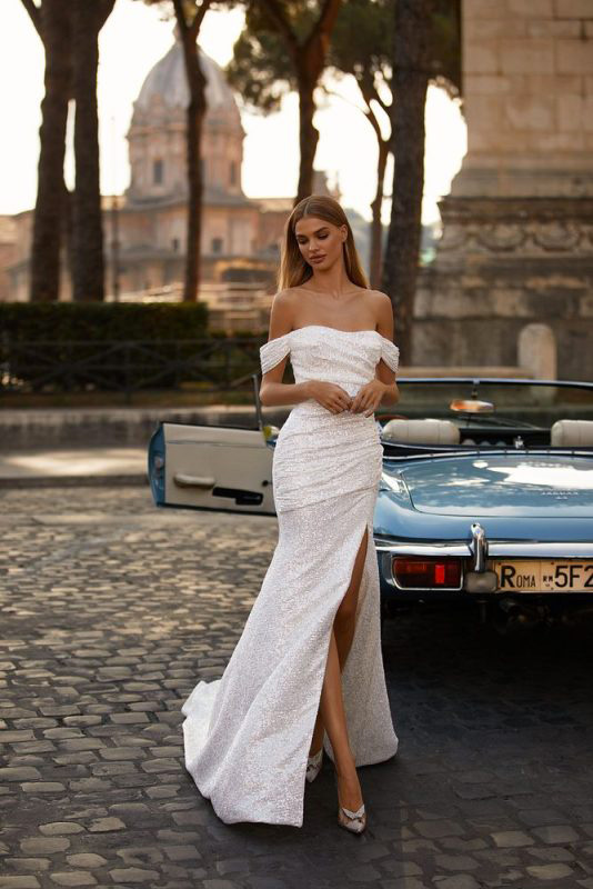 In questa foto una modella indossa un abito da sposa off white, a sirena con spacco, della collezione Millanova 2023 