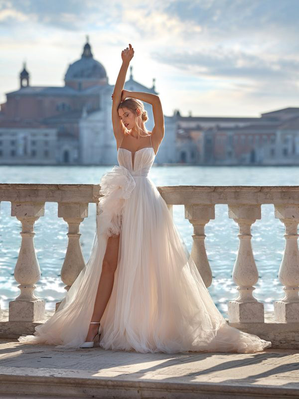 In questa foto il modello di punta della collezione di abiti da sposa 2023 di Nicole Milano. Il vestito ha delle sfumature rosa pastello e un maxi fiocco sulla vita