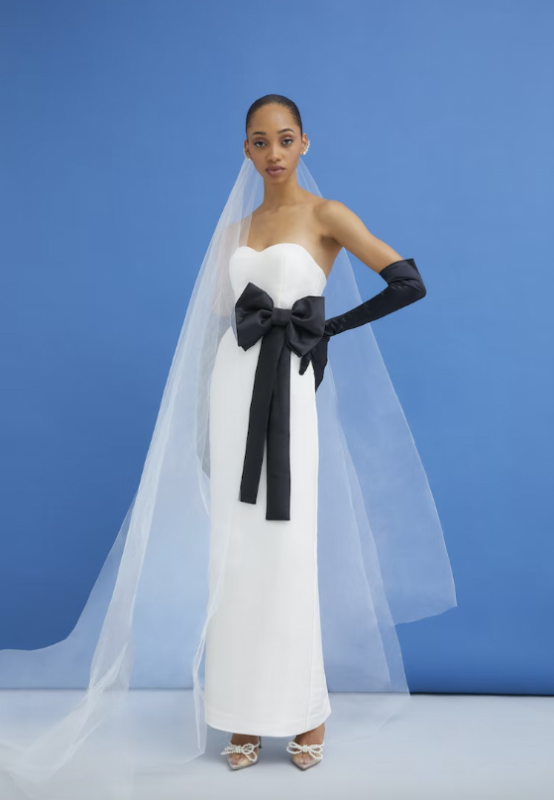 In questa foto una modella indossa un abito da sposa con maxi fiocco in vita e guanti neri della collezione Scorcesa 2023