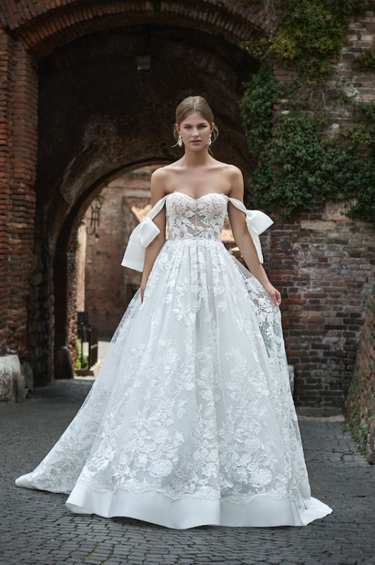 In questa foto una modella cammina indossando un abito da sposa romantico, con fiocchi sulle spalle, della linea Victoria 2023 del brand Maison Signore