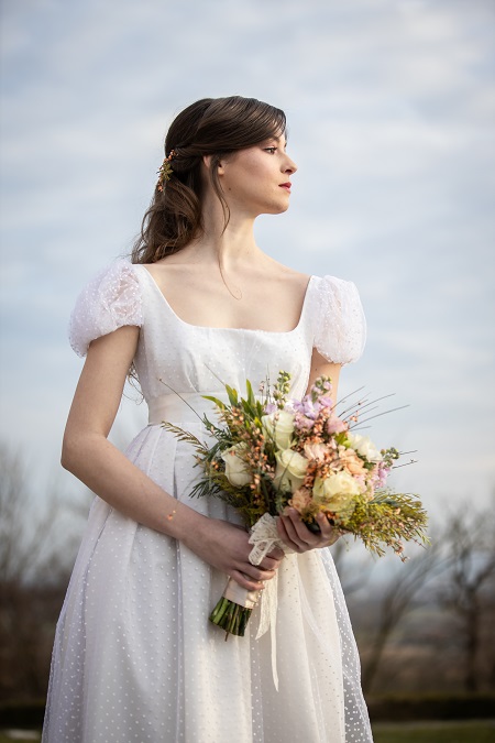 In questa foto, una sposa indossa un abito stile impero con nastro bianco in vita e dettagli in organza con lavorazione a pois perfetto per un matrimonio stile Bridgerton