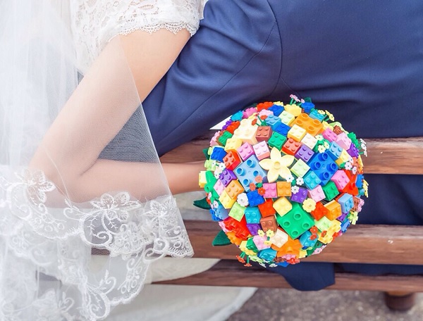 In questa foto, si intravede una coppia di sposi ripresa di spalle, la sposa tiene in mano un bouquet di fiori Lego