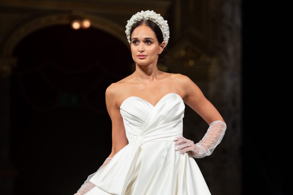 In questa foto la modella indossa un abito da sposa strutturato con guanto trasparente.