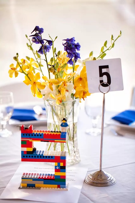 In questa foto, un centrotavola floreale completato dal numero del tavolo riprodotto in piccolo su carta e in versione più grande con i mattoncini Lego 