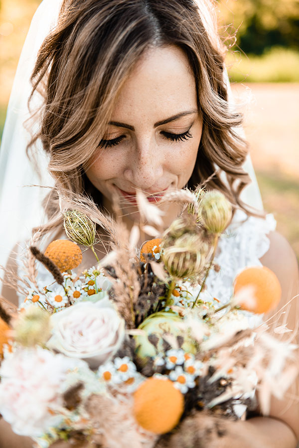 in questa foto un bouquet da sposa eco-friendly con margherite, spighe di grano, rametti e altri fiori spontanei