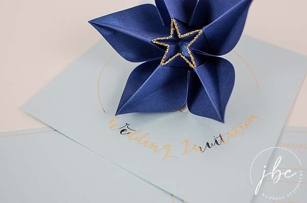 In questa foto, partecipazioni matrimonio originali con fiore origami color indaco e dettagli dorati