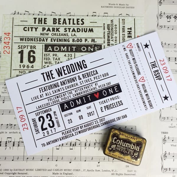 In questa foto, partecipazioni matrimonio originali che riproducono il biglietto d'ingresso a un concerto con sfondo bianco, scritta nera e dettagli in rosso