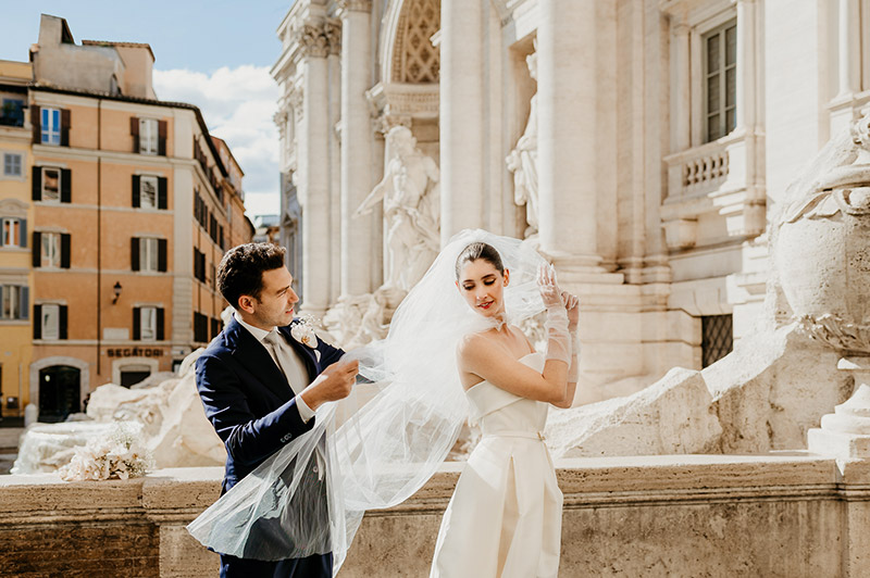 In questa foto una coppia di sposi a Roma: lui le si sistema il velo