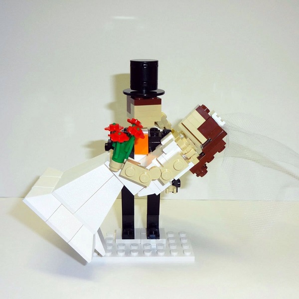 In questa foto, un cake topper creato con mattoncini Lego in cui lo sposo tiene in braccio la sposa 