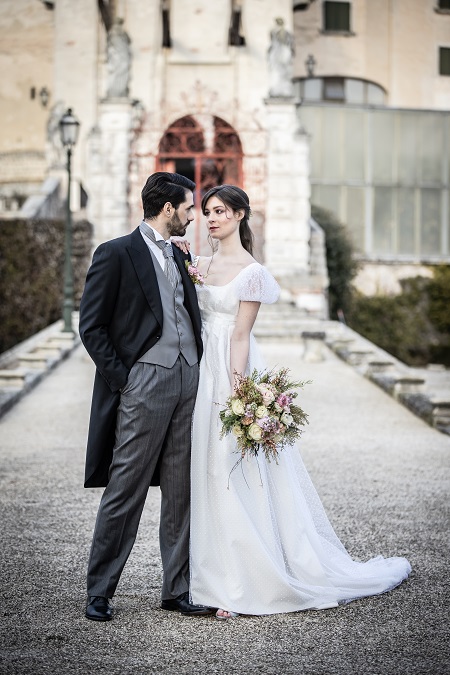 In questa foto, una coppia di sposi che si guardano, lei indossa un abito di organza e lui un tight spezzato 