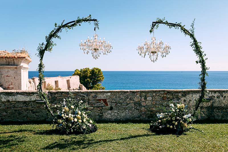 In questa foto due chandelier di cristallo appesi a due strutture verticali ad arco ricoperte di piante rampicanti
