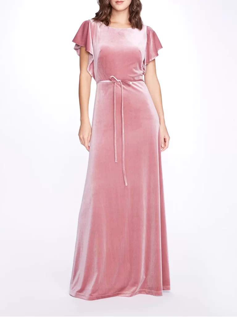 In questa foto una modella indossa uno degli abiti da cerimonia in velluto di colore rosa di Marchesa. Il modello è lungo con manica corta morbida e nastro sottile con fiocchetto 