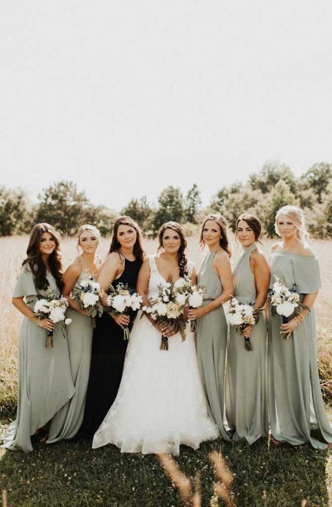 In questa foto una sposa con abito in pizzo a A posa con le sue damigelle che indossano abiti da cerimonia donna di colore verde menta. La damigella d'onore indossa un abito diverso di colore marrone scuro