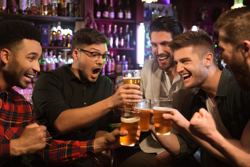 In questa foto lo sposo brinda e ride con i suoi amici in un pub con bicchieri di birra 
