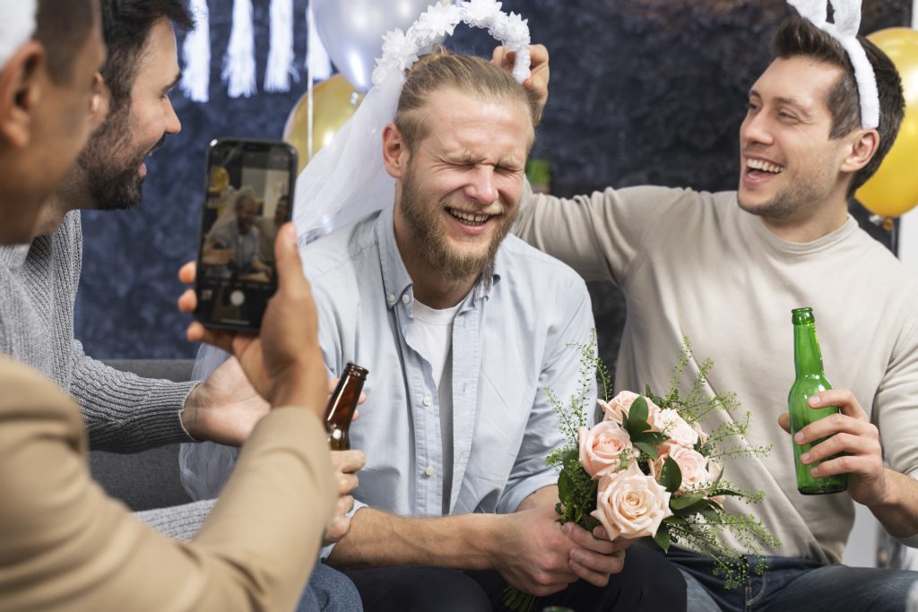 In questa foto uno scherzo per addio al celibato: lo sposo viene travestito da sposa con velo e bouquet mentre gli amici gli scattano foto con il cellulare