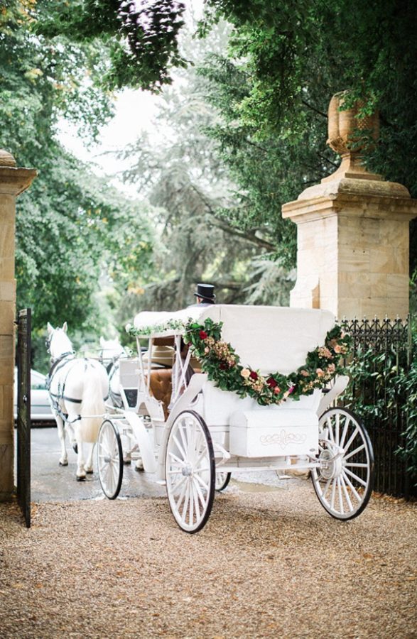 In questa foto una carrozza con cavalli per matrimonio di colore bianco decorata con un tralcio di fiori e foglie sul retro