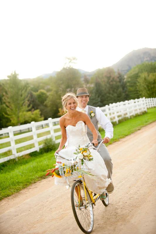 In questa foto due sposi sorridenti a bordo di una bicicletta per matrimonio di colore giallo