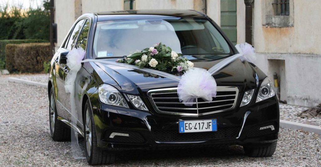 In questa foto una Mercedes per matrimonio decorata con fiori e coccarde di tulle sul cofano anteriore e sugli specchietti