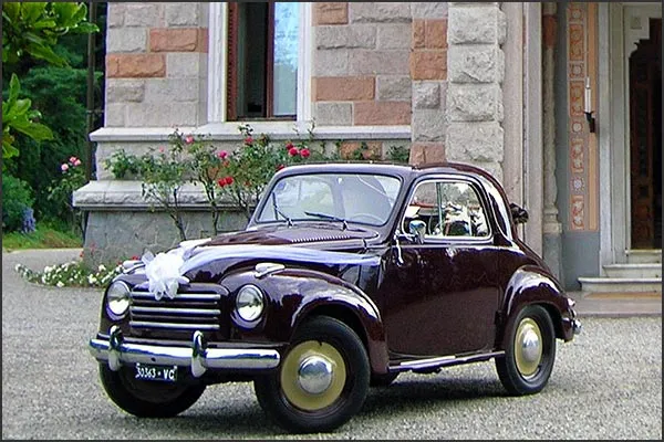 In questa foto una Fiat Topolino di colore bordeaux per matrimonio decorata con una coccarda sul cofano anteriore
