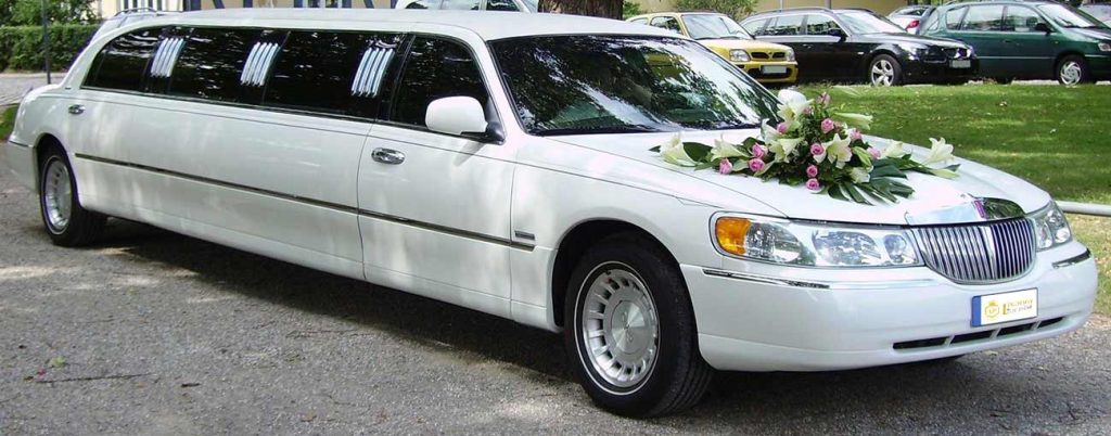 In questa foto una limousine per matrimonio di colore bianco decorata con una composizione di fiori sul cofano anteriore