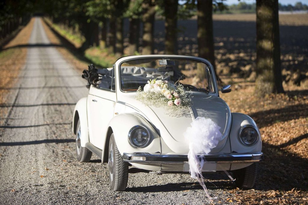 In questa foto una maggiolino cabrio per matrimonio di colore bianco decorato con una coccarda bianca e una composizione di fiori