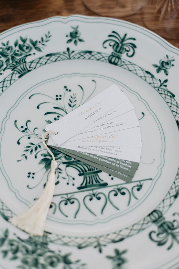 In questa foto un menù di nozze a ventaglio di colore bianco e verde bosco poggiato su un piatto di ceramica