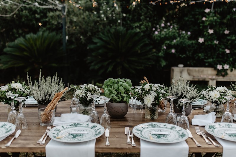 In questa foto il dettaglio di una mise en place per matrimonio con piatti di porcellana, tovaglioli di lino, vasetti con grissini ed erbe aromatiche