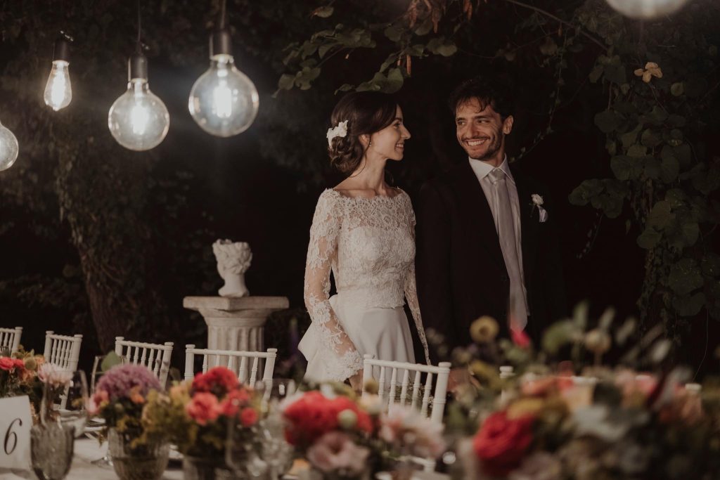 In questa foto una coppia di sposi si scambia un tenero sorriso di fronte ai tavoli decorati dalle creazioni di Maria Mannino Floral Designer