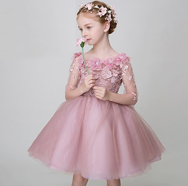 In questa foto, una bambina indossa un abito da damigella con gonna ampia di tulle e corpetto con decori floreali rosa 