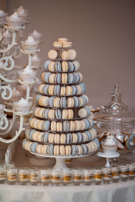 In questa foto, in primo piano un'alzatina di macaron color crema e azzurro polvere decorano l'angolo dolci di un matrimonio stile Bridgerton 