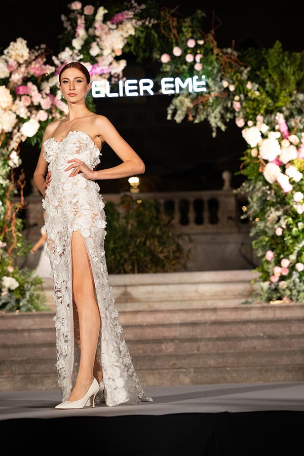 In questa foto una modella sfila indossando un abito da sposa a sirena di Atelier Emé con spacco, scollo a cuore senza spalline e fiori 3D