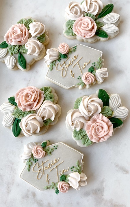 In questa foto, biscotti nuziali con dettagli floreali e le iniziali degli sposi nei toni del bianco, rosa, verde chiaro e scuro