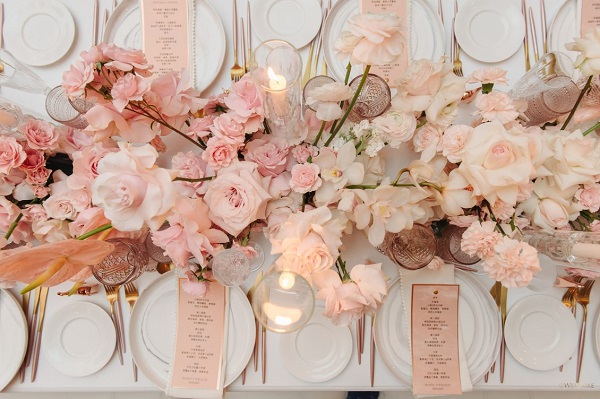 In questa foto, un centrotavola floreale con bicchieri e menu poggiati sui piatti dello stesso colore 