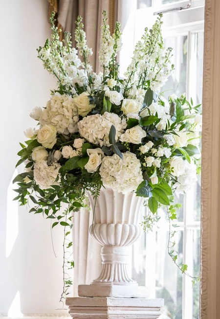 In questa foto, una composizione floreale di ortensie, rose e altri fiori total white sistemata all'interno di un vaso bianco in stile neoclassico