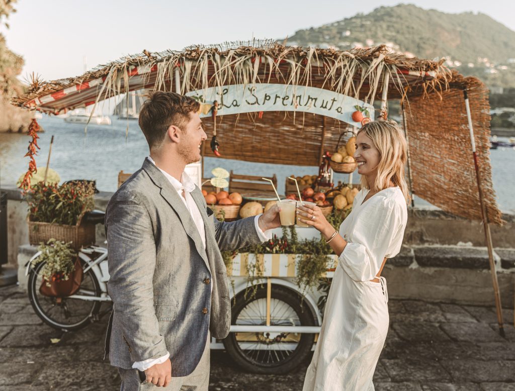 In questa foto una coppia di sposi brinda con una spremuta davanti ad un carretto della tradizione siciliana