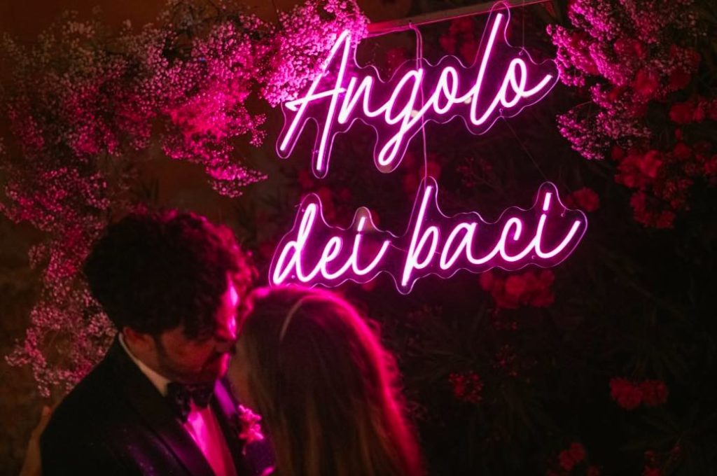 In questa foto la scritta neon fucsia "Angolo dei baci", con cui gli sposi hanno allestito il loro Photo Booth