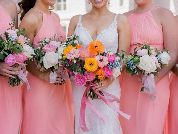 In questa foto, si intravedono al centro una sposa in abito bianco e accanto le damigelle adulte con abiti rosa brillante con in mano bouquet simili a quello della sposa