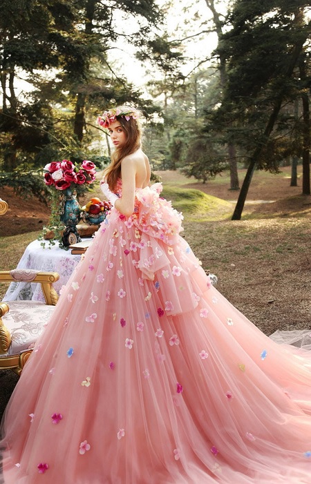 In questa foto, una modella di profilo, fotografata in un bosco, indossa un abito da sposa rosa brillante con gonna ampia di tulle e dettagli floreali