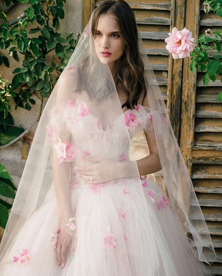 In questa foto, una modella indossa un abito da sposa bianco in tulle con fiori rosa brillante, il colore della Biodiversità di Pantone 