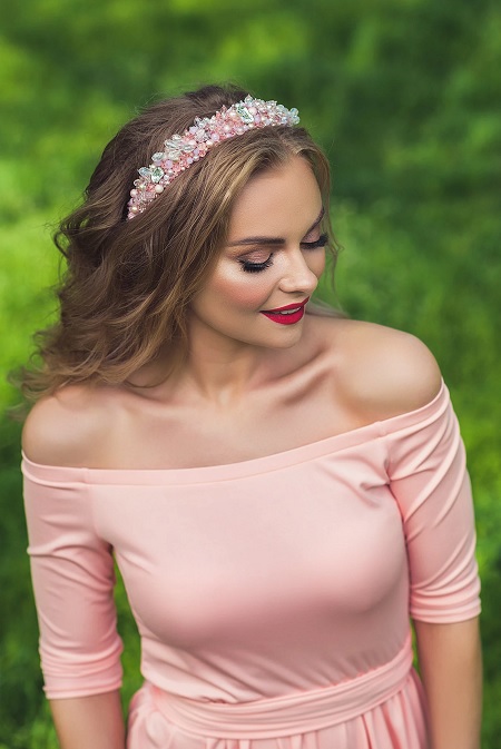 In questa foto, una modella, fotografata a mezzo busto e dall'alto, indossa un abito rosa e un cerchietto gioiello con cristalli argento, bianchi e rosa brillante 
