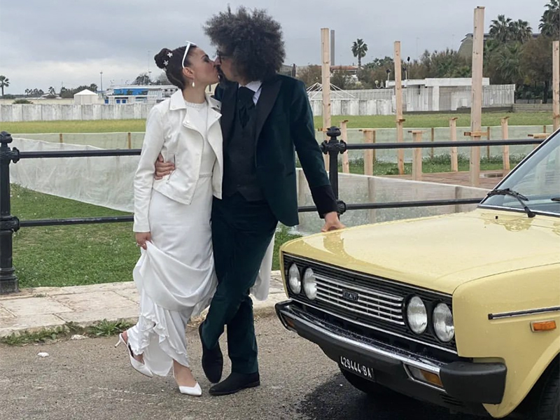 Caparezza e Albina durante il loro matrimonio si baciano vicino la macchina vintage gialla