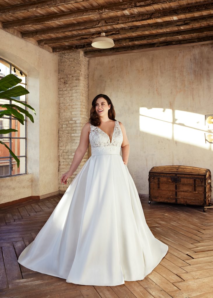 Uno degli abiti da sposa curvy 2023 che fa parte della nuova collezione sposa Modeca. Un modello con corpetto in pizzo e ampia gonna.