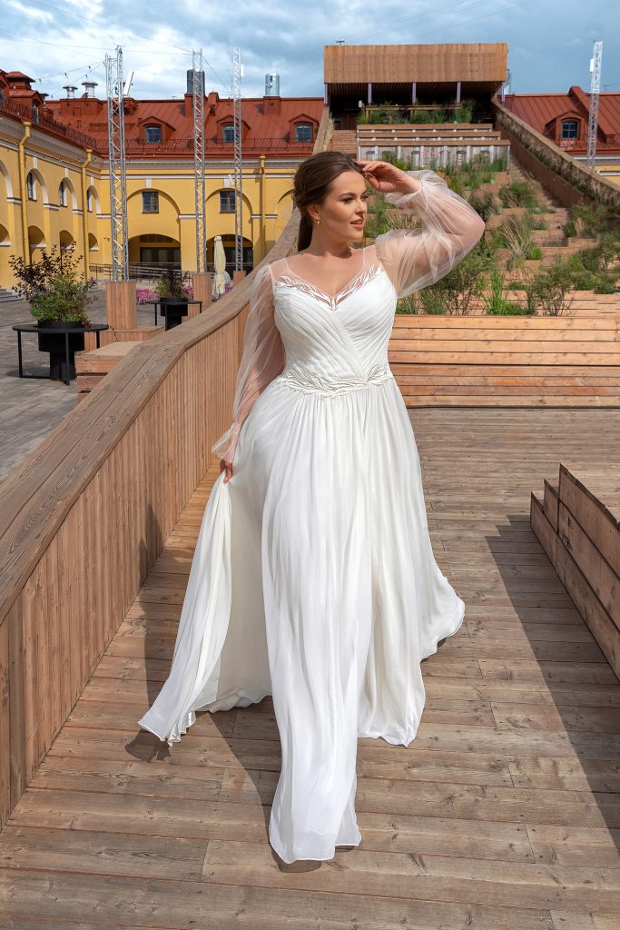 Uno degli abiti da sposa curvy 2023 che fa parte della nuova collezione sposa Papilio. Un modello dai tessuti leggeri e maniche in tulle. 