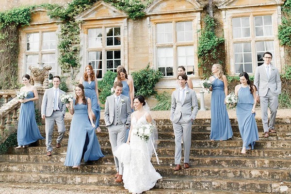 In questa foto, su una scalinata al centro la sposa in abito bianco, lo sposo in abito grigio chiaro, damigelle in abito azzurro polvere e accompagnatori in grigio chiaro 