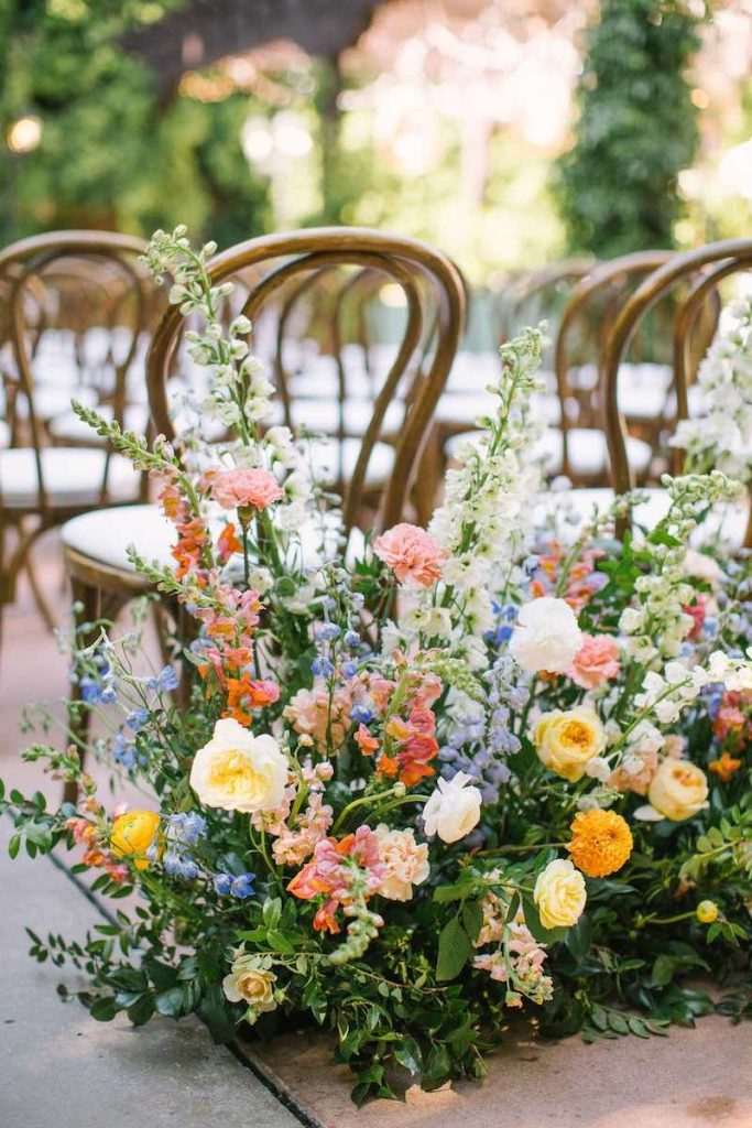 In questa foto una composizione di fiori per una cerimonia di nozze in stile shabby chic realizzata con roselline di colore rosa, giallo, ranuncoli e fiori di colori azzurro e arancione