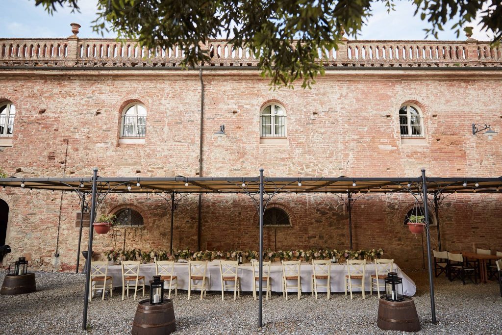 In questa foto un lungo tavolo imperiale allestito per un ricevimento di nozze sotto la tettoia esterna del ristorante di Borgo Colleoli