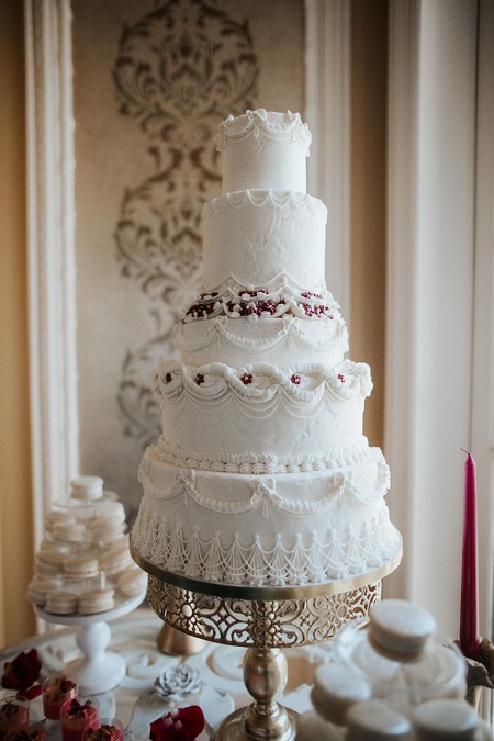In questa foto, una torta nuziale a più piani realizzata con ghiaccia reale e decori di zucchero pensata per un matrimonio stile Bridgerton 