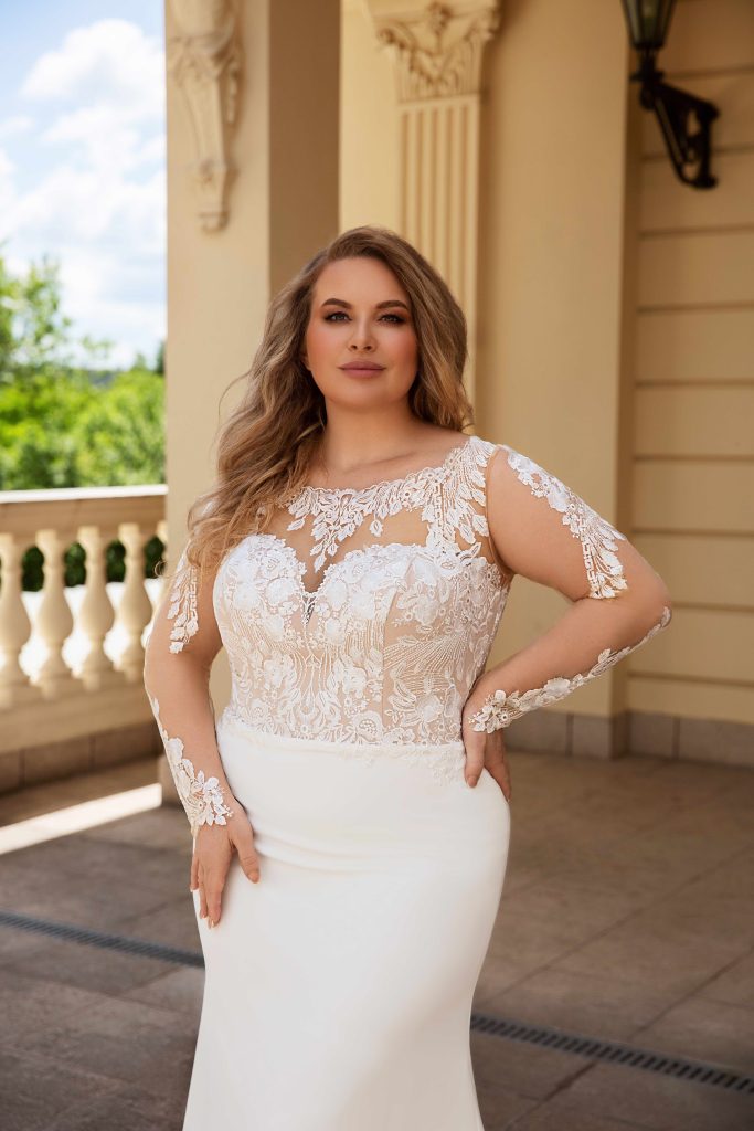 Uno degli abiti da sposa curvy 2023 che fa parte della nuova collezione sposa Monica Loretti. Un modello con corpetto in pizzo e maniche tatuaggio.